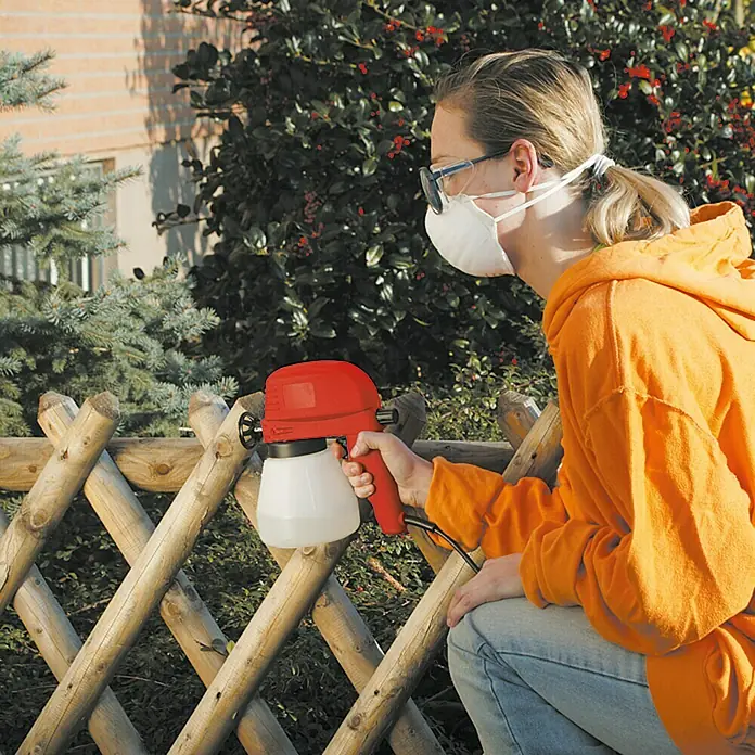 Lehnartz Elektrische Spritzpistole Easy-Sprayer PLUS - 45 W - Frau sprüht mit einer roten Farbspritzpistole einen Holzzaun. Die Spritzpistole liegt gut in der Hand und ist leicht zu bedienen.