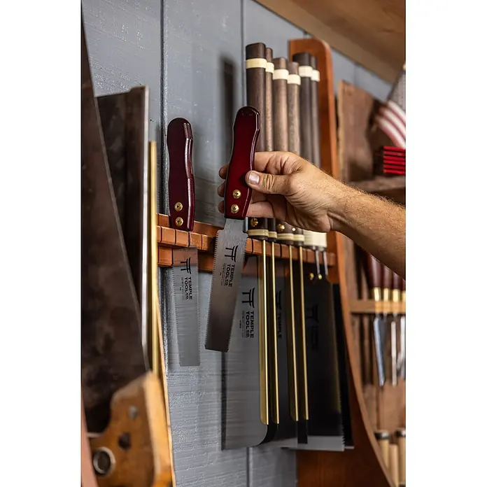 Temple Tool Japansäge Flush Cut - Blattlänge: 150 mm - Hand greift nach einer japanischen Zugsäge mit rotem Holzgriff und Metallklinge, aufbewahrt mit anderen Holzbearbeitungswerkzeugen.