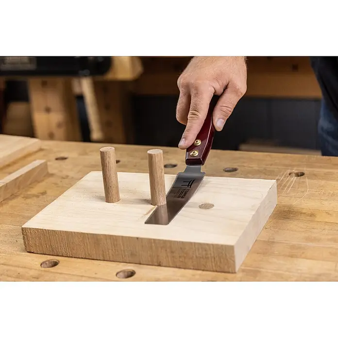 Temple Tool Japansäge Flush Cut - Blattlänge: 150 mm - Eine Person verwendet eine Handsäge mit rotem Griff, um eine präzise Nut in einen hellen Holzklotz zu schneiden, der von zwei Dübeln gehalten wird.