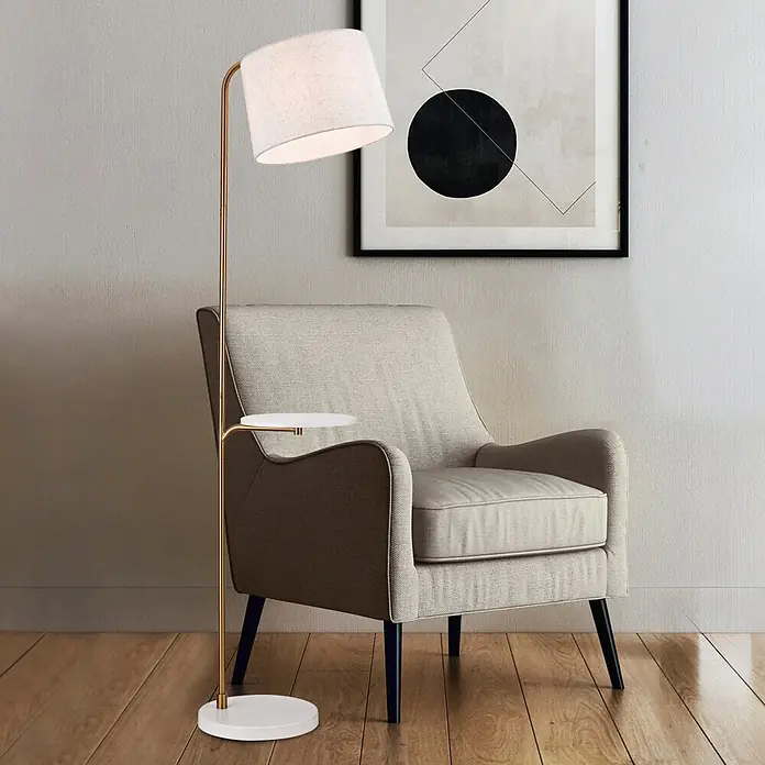 Alemar Lámpara de pie Tau - 60 W, Latón, Altura: 160 cm, Color pantalla: Beige - Lámpara de pie con acabado de latón, pantalla de tela blanca y mesa auxiliar blanca integrada, junto a un sillón.
