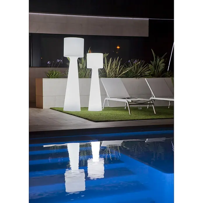 New Garden Lámpara de pie para exterior Grace 140 - Blanco cálido, Con bombillas - Dos lámparas de pie blancas y luminosas están sobre césped artificial junto a una piscina de noche. Sus reflejos son visibles en el agua azul.