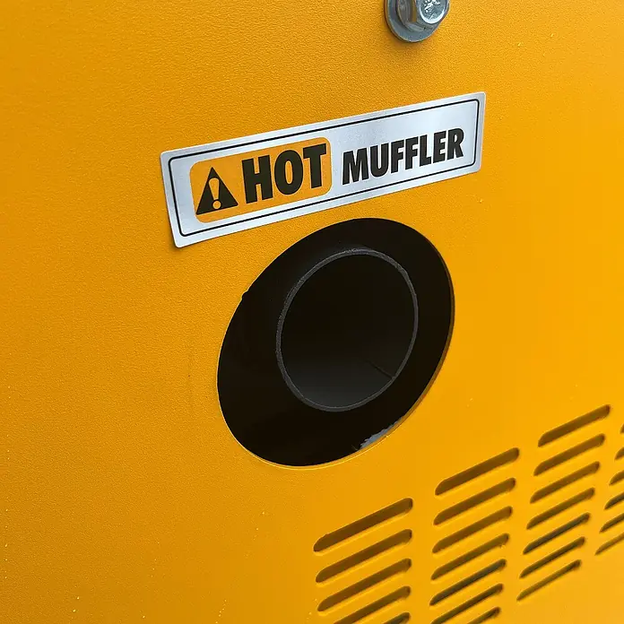 KIPOR Stromerzeuger Diesel AVR Stromerzeuger 16 kW / 20 kVA - KIPOR DG20000 - Nennleistung: 16 kW, Tankvolumen: 30 l - Warnaufkleber "HOT MUFFLER" mit Warnsymbol über schwarzem Auspuffrohr an einer texturierten gelben Maschinenverkleidung.