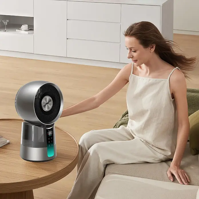 Climatizador evaporativo TF414 DREO - Gris, 35 W - Una mujer ajusta un ventilador humidificador plateado y gris con pantalla digital sobre una mesa de madera en la sala.