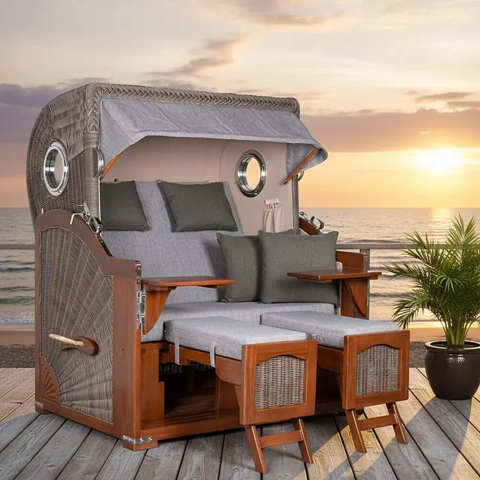 Mr. Deko Strandstuhl Strandkorb Düne Grande Bullauge Mahagoni PE Grey Dessin 570 - Teakholz. Polyrattan, Rückenlehne verstellbar, Grau, B x T x H: 142 x 95 x 170 cm - Ein luxuriöser Strandkorb aus geflochtenem Rattan mit hellgrauen Kissen und dunklen Holzdetails steht auf einem Deck mit Meerblick bei Sonnenuntergang.