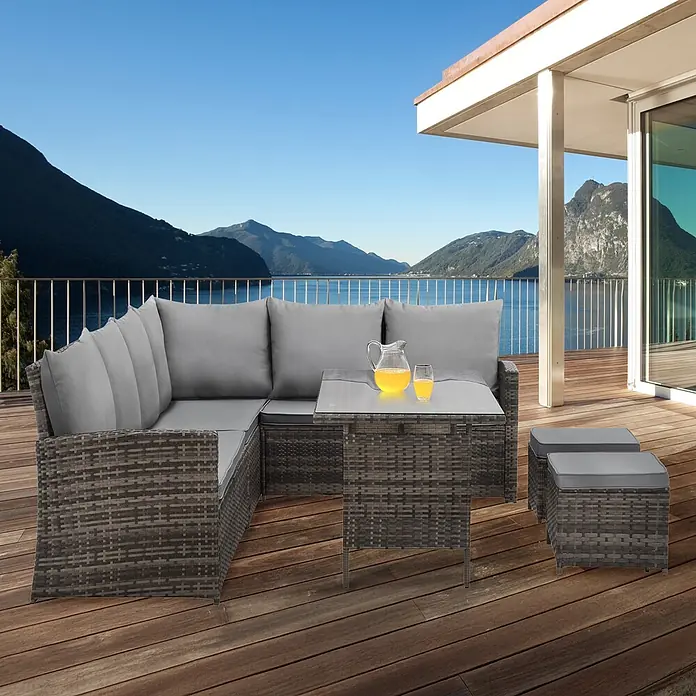 SVITA Loungemöbel-Set MONROE - 4 -tlg., Polyrattan, Braun - Ein graues Rattan-Gartenmöbelset mit Ecksofa, Couchtisch und zwei Hockern auf einer Holzterrasse mit Seeblick.