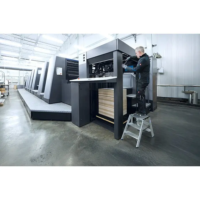 Krause Doppel-Klapptritt 2X4 Stufen - Anzahl Tritte: 8 Stk., Belastbarkeit: 225 kg, Aluminium - Silberne Aluminium-Stehleiter in Industrieumgebung, von Arbeiter an großer Druckmaschine genutzt.
