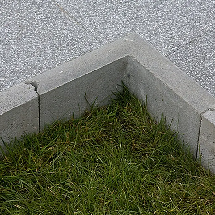EHL Rasenkante Ecke - Grau, Beton - Betoneinfassung mit Rasenfüllung. Robuste graue Steine bilden eine Ecke und grenzen einen Rasenbereich von einem grauen Steinpflaster ab.
