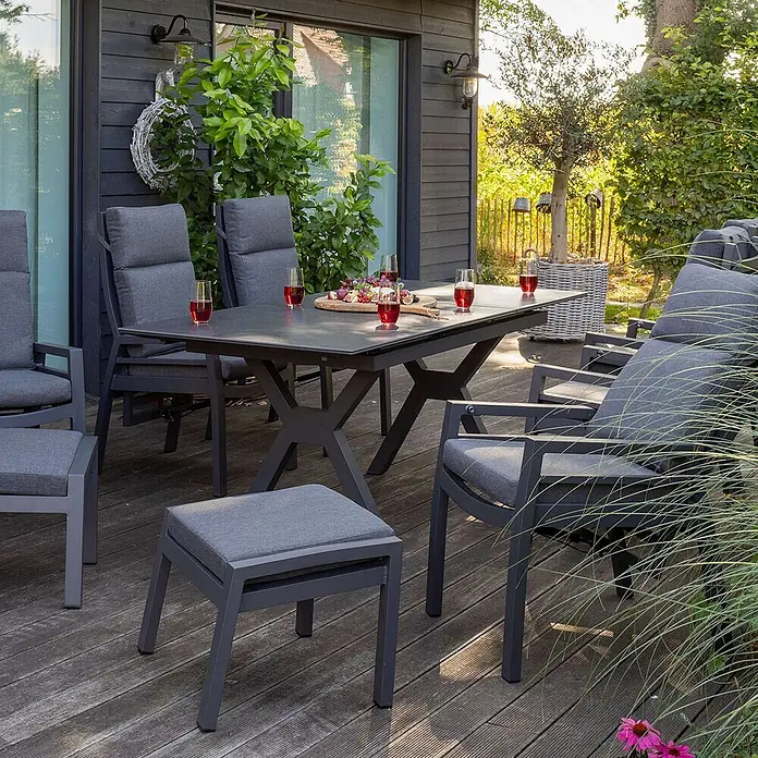 Bene Living Gartentisch-Set Merida + Hocker mit Tisch Granada - Gesamtumfang: 9 -tlg., Aluminium pulverbeschichtet, Textilene, Keramik, Ausziehbar - Dunkelgraue Outdoor-Essgruppe mit Tisch, Stühlen und Hocker auf einer Holzterrasse.