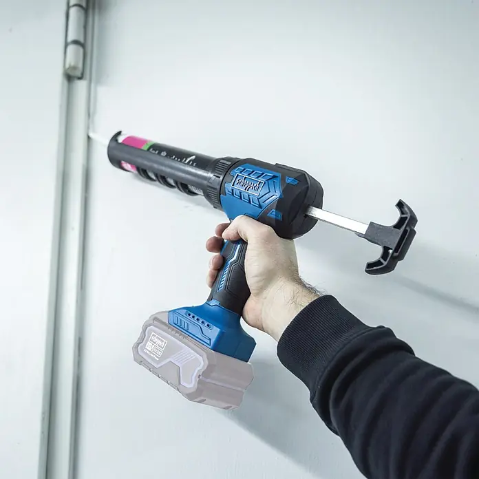 Scheppach IXES 20V Akku-Kartuschenpresse C-SEG310-X - 20 V, Ohne Akku - Hand verwendet eine blau-schwarze Akku-Dichtpistole, um weißen Dichtstoff auf eine Fuge aufzutragen.