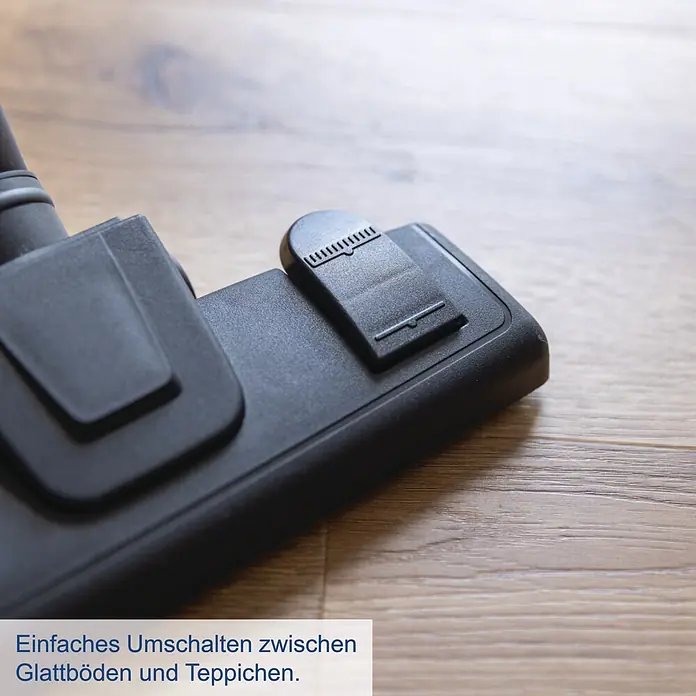 Scheppach IXES 20V Akku-Handstaubsauger C-HVC150-X - 20 V, Ohne Akku, Behältervolumen: 0,56 l - Schwarze Staubsaugerdüse aus Kunststoff mit Umschalter für Glattböden und Teppiche, auf einem Holzboden.