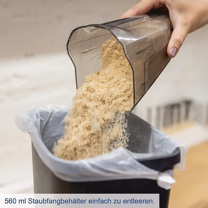 Scheppach IXES 20V Akku-Handstaubsauger C-HVC150-X - 20 V, Ohne Akku, Behältervolumen: 0,56 l - Eine Hand entleert Sägemehl aus einem transparenten 560 ml Staubfangbehälter in einen Mülleimer.