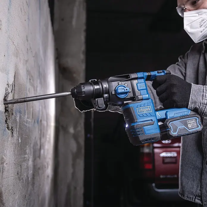 Scheppach IXES 20V Akku-Kombihammer - 20 V, Ohne Akku, 2,8 J - Person bohrt mit einem blau-schwarzen Akku-Bohrhammer in eine Betonwand.