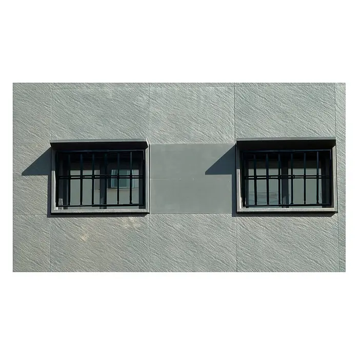Adaptta Fenstergitter ausziehbar 55×95–100×165 cm, schwarz - B x H: 55 x 95 cm, Auszugslänge: 165 cm, Montage Fenstergitter: Fensterlaibungsmontage - Zwei vergitterte Fenster an einer hellgrauen, strukturierten Wand. Schatten verleihen der Fassade Tiefe.