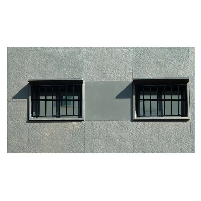 Adaptta Fenstergitter ausziehbar 55×55–100×100 cm, schwarz - B x H: 55 x 55 cm, Auszugslänge: 100 cm, Montage Fenstergitter: Fensterlaibungsmontage - Zwei rechteckige Fenster mit dunklen Sicherheitsgittern an einer grauen, strukturierten Gebäudewand. Ein glattes graues Paneel ist dazwischen und darunter.