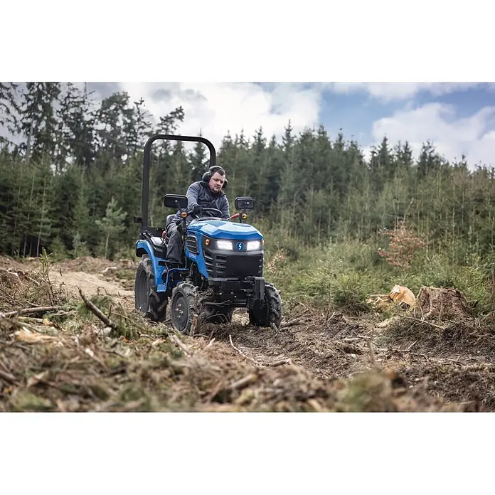 Scheppach Kleintraktor MT25 - Hubraum: 1.132 cm³, Tankvolumen: 10 l - Blauer Kompakttraktor wird von einer Person in einer Waldlichtung mit Baumresten gefahren.