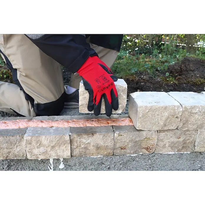 Beko Klebeschaum E-Glue - 810 ml - Rote und schwarze Arbeitshandschuhe legen einen hellen Steinblock auf orangefarbenen Bauschaum für den Mauerbau.