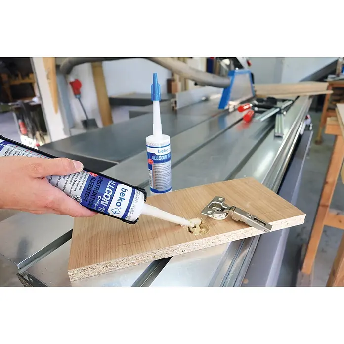 Beko Konstruktionskleber Allcon 10 - 150 ml, Beige - Eine Hand trägt weißen Beko ALLCON 10 Konstruktionsklebstoff aus einer blau-weißen Tube in ein gebohrtes Loch in einer Holzplatte auf; weitere Tube im Hintergrund.