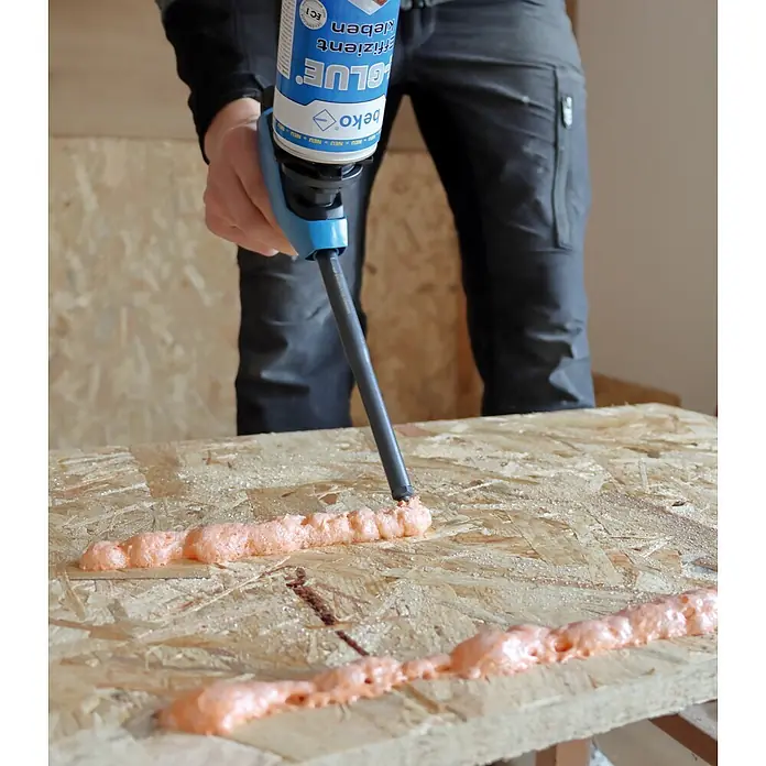 Beko Klebeschaum E-Glue - 810 ml - Person trägt orangefarbenen Beko GLUE Montageschaum mit einer Pistole auf eine OSB-Platte auf.