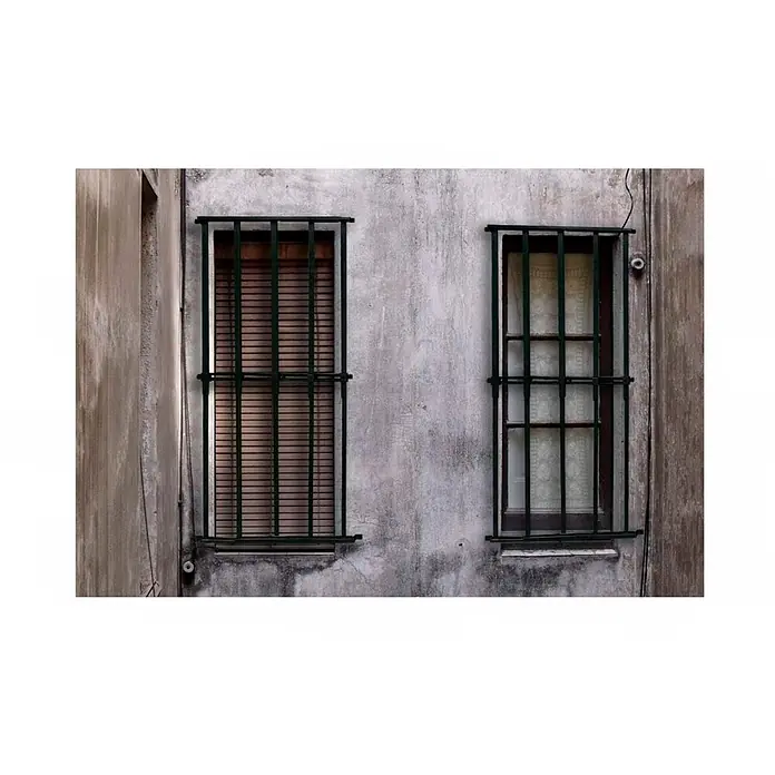 Adaptta Fenstergitter ausziehbar 55×95–100×165 cm, schwarz - Montage Fenstergitter: Fensterrahmenmontage - Zwei rechteckige Fenster mit dunklen Metallgittern an einer verwitterten Gebäudefassade. Ein Fenster hat geschlossene Jalousien, das andere einen Gardine.