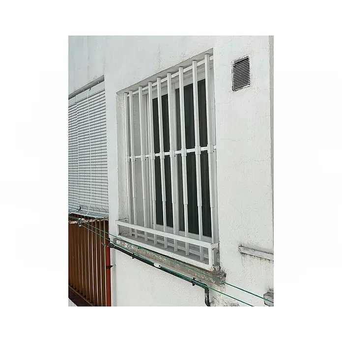 Adaptta Fenstergitter ausziehbar 55×55–100×100 cm, weiß - B x H: 55 x 55 cm, Auszugslänge: 100 cm, Montage Fenstergitter: Fensterlaibungsmontage - Weiße Fenstergitter schützen ein Fenster neben einem weißen Rollladen an einer Gebäudefassade.