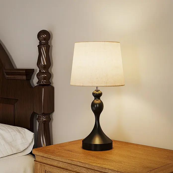 Homcom Tischleuchte - 40 W, L x B x H: 28 x 28 x 54 cm, Schwarz, Cremeweiß, E27 - Eine Tischlampe mit schwarzem Fuß und hellem Stoffschirm, die einen Holznachttisch neben einem dunklen Holzbett beleuchtet.