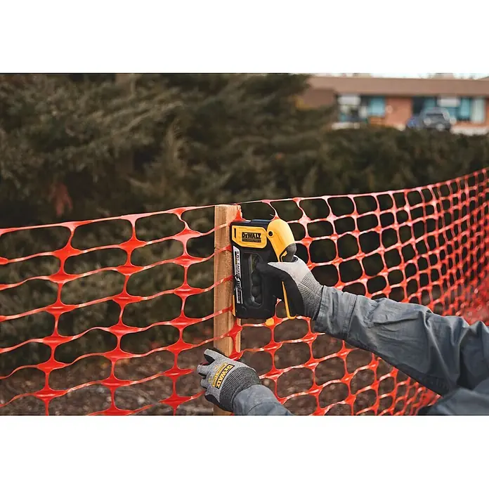 DeWalt Grapadora manual DWHT70510 - Profundidad de grapado: 6 mm - 14 mm - Persona usando una engrapadora DeWalt amarilla y negra para fijar una valla de construcción naranja a un poste de madera.