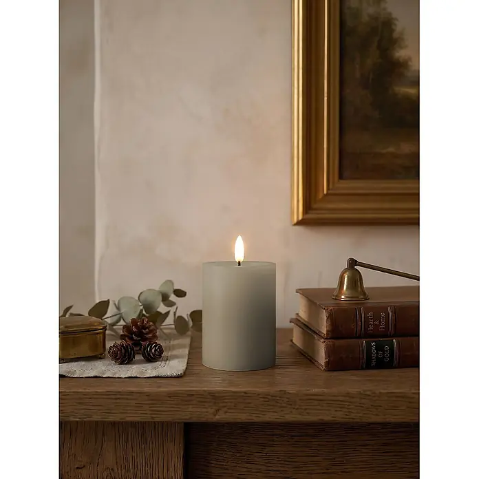LED-Kerze Novita - Taupe, Ø x H: 7,5 x 10 cm, Echtwachs - Graue Stumpenkerze mit realistischer flackernder Flamme, Teil einer gemütlichen, rustikalen Innendekoration auf einem Holzkamin.