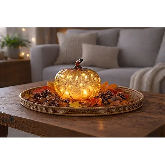 LED-Dekofigur Dekokürbis - L x B x H: 15 x 15 x 13 cm - Beleuchteter Kürbis aus bernsteinfarbenem Glas auf Tablett mit Herbstblättern und Tannenzapfen auf Couchtisch.