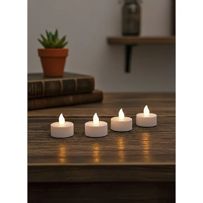 LED-Teelicht Nele - 4 Stk., Weiß, Ø x H: 3,8 x 3,5 cm - Vier weiße LED-Teelichter mit warm flackernden Flammen auf einem dunklen Holztisch, die eine gemütliche Atmosphäre schaffen.