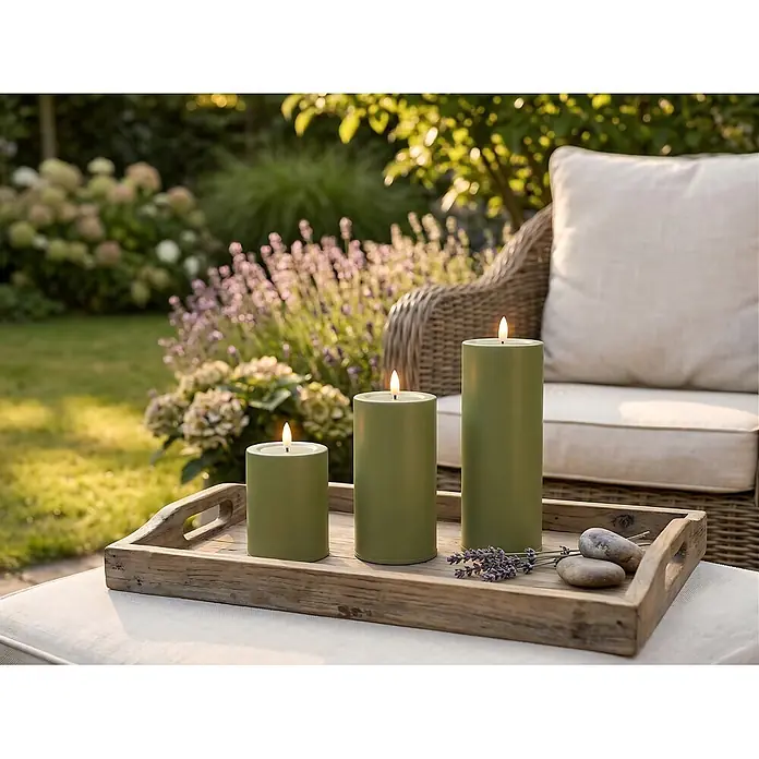 LED-Kerze Niumi - Ø x H: 8 x 10 cm, Salbei, Metall - Drei grüne Stumpenkerzen mit flackernden Flammen auf einem Holztablett, mit Lavendel und Kieselsteinen, in einem Gartensetting.