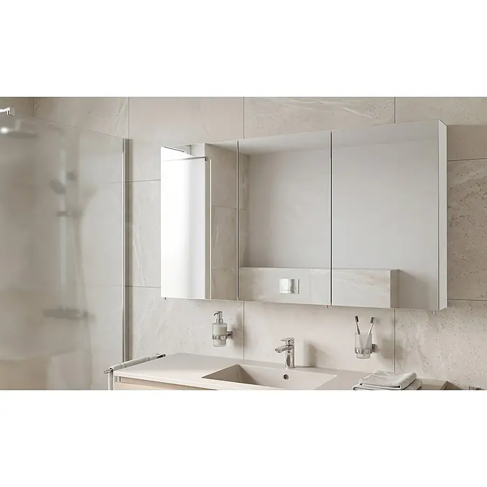 Schildmeyer Spiegelschrank Basic - B x H: 120 x 70,7 cm, Holz - Spiegelschrank mit drei Türen über einem Waschbecken mit Armatur, Seifenspender und Zahnbürstenhalter in einem modernen, hell gefliesten Badezimmer.