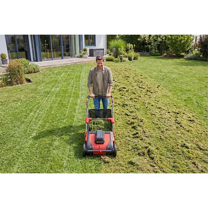 Einhell PXC 18V Laubsammler GE-GC 18/55 Li - Ohne Akku, 18 V, 100 l - Mann benutzt roten und schwarzen Elektro-Vertikutierer auf Rasen, mit vertikutierten und unvertikutierten Bereichen.