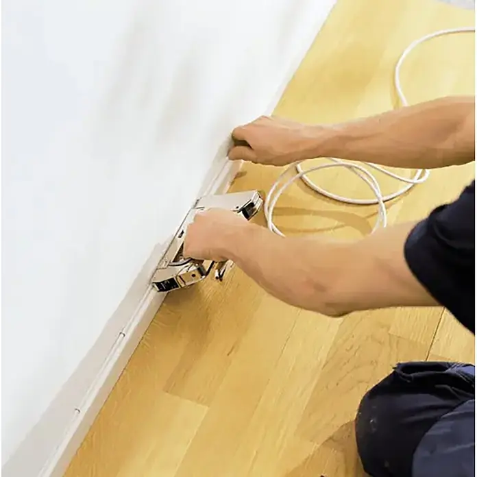 Rapid Grapadora de cables Pro R36 - Apto para: Cable hasta Ø 6 mm, Profundidad de grapado: 10 mm - 14 mm - Mano usando una grapadora para fijar una tira blanca de gestión de cables a la pared.