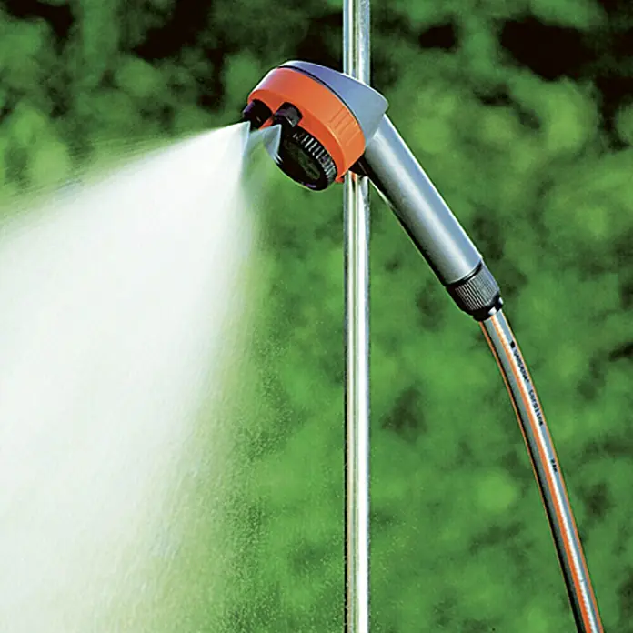Gardena Gartendusche Trio - Dreibeinstativ, Höhe: 220 cm, Aluminium/Kunststoff - Nahaufnahme eines Gardena Duschkopfes, der Wasser versprüht, befestigt an einer Stange. Der Duschkopf ist grau und orange.