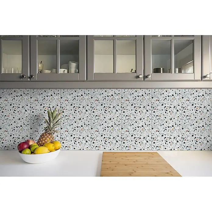 Tulup Wandfliese - Glänzend - Weiße Terrazzo-Fliesen mit bunten Sprenkeln als Küchenrückwand über einer Arbeitsplatte.