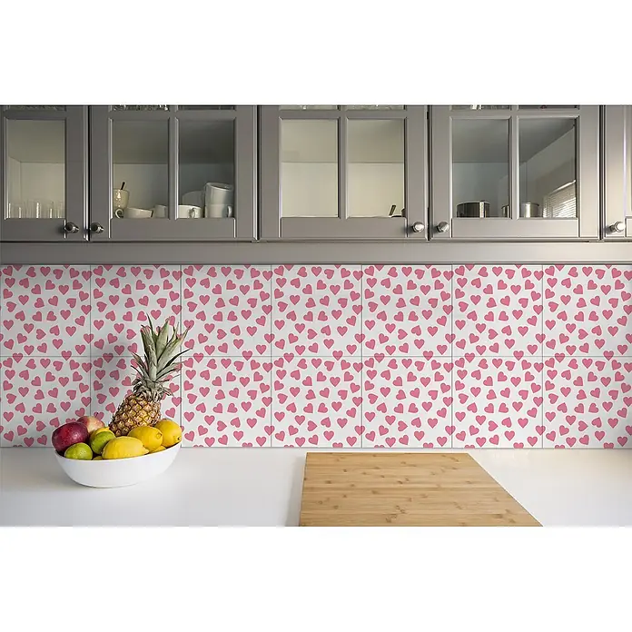 Tulup Wandfliese - Glänzend - Weiße Küchenfliesen mit verspieltem rosa Herzmuster, als Spritzschutz unter grauen Schränken und über einer weißen Arbeitsplatte.