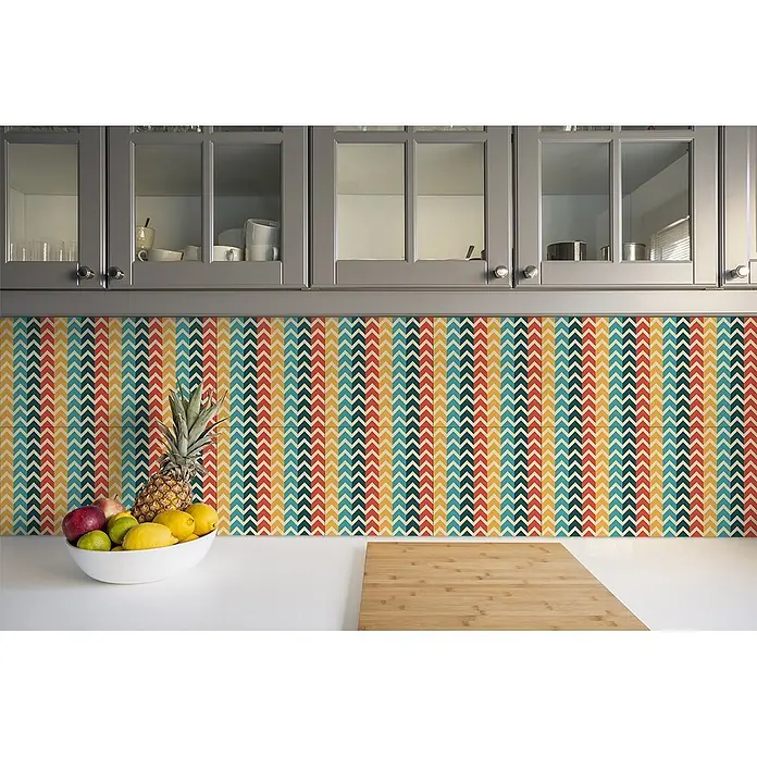 Tulup Wandfliese - Glänzend - Küchenrückwand mit farbenfrohem Chevron-Muster in Rot, Gelb, Petrol und Beige, unter grauen Schränken über einer weißen Arbeitsplatte.