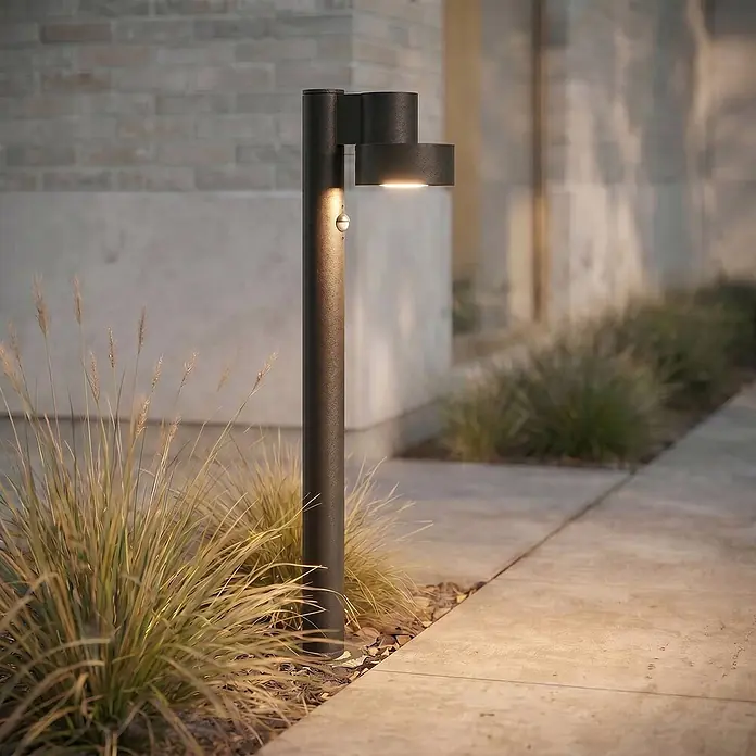 Lucande LED Wegeleuchte in schwarz matt, mit Bewegungsmelder, Gartenlampe -  - Dunkelgraue Wegeleuchte mit integriertem Sensor, beleuchtet einen modernen Außenweg und Ziergräser.