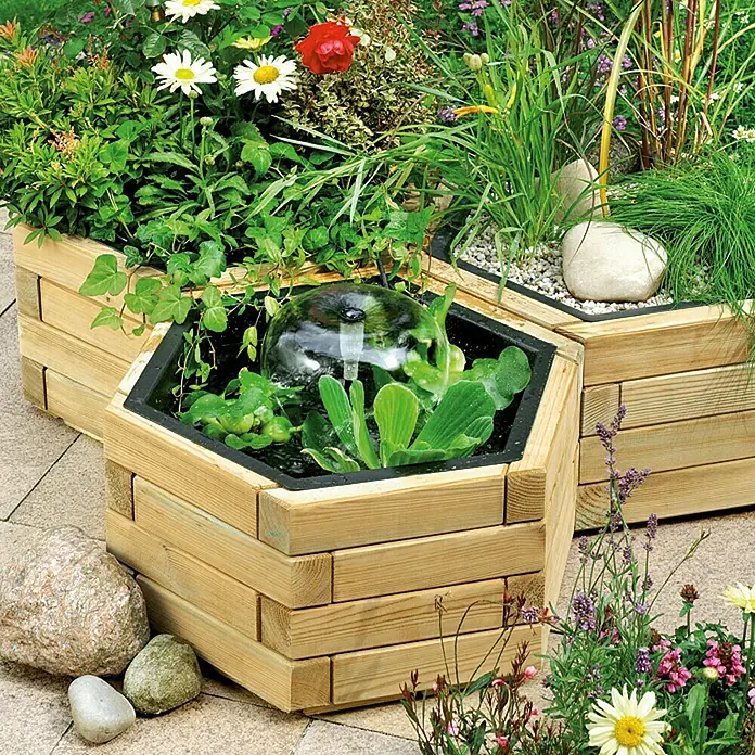 Pflanztopf Carina - Außenmaß (Ø x H): 60 x 29 cm, Holz - Holzkästen mit Pflanzen und einem Wasserfontäne-Element. Ideal für Garten und Terrasse, bringt natürliche Schönheit ins Freie.
