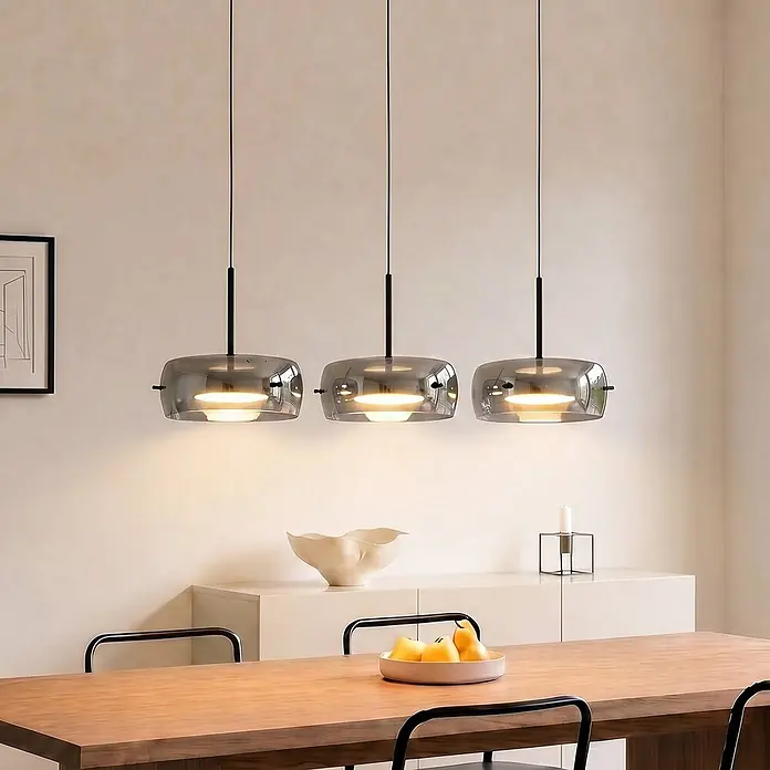 Lucande LED Pendelleuchte in schwarz, dimmbar Hängelampe -  - Drei moderne Pendelleuchten mit Rauchglasschirmen und schwarzen Akzenten, die einen Esstisch beleuchten.