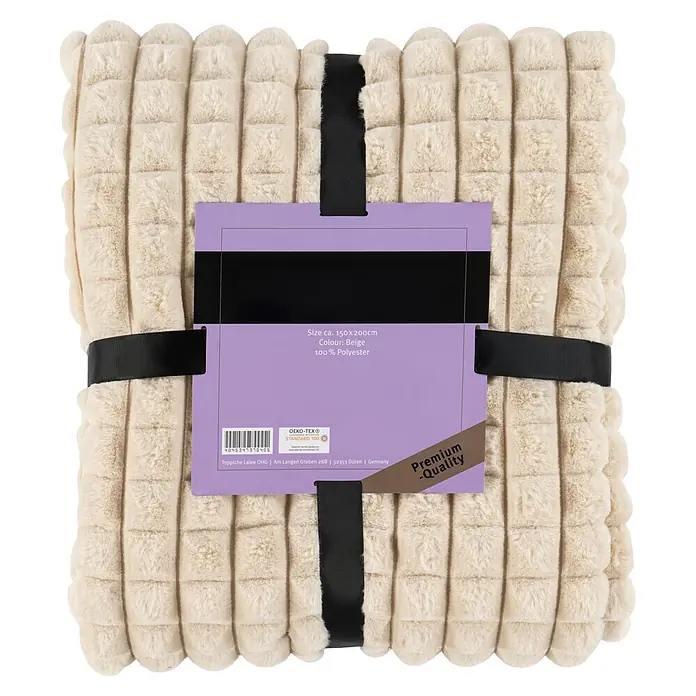 Wohndecke Spa Essence 125 - 150 x 200 cm, Beige, 100 % Polyester - Beige Plüschdecke mit strukturierter Waffelprägung, ordentlich gefaltet und mit einem schwarzen Band sowie lila Etikett umwickelt.