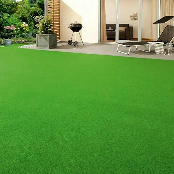 Rasenteppich Meterware Green - Breite: 150 cm, Grün, Mit Drainagenoppen - Grüner Rasen auf einer Gartenterrasse mit Grill, Liegestuhl und Bepflanzung im Hintergrund für entspannte Stunden im Freien.