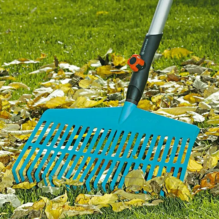 Gardena Combisystem Rechenbesen - Arbeitsbreite: 43 cm, Kunststoff - Ein blauer Gardena Rechen liegt auf dem Rasen zwischen gelben Blättern. Ideal, um den Garten sauber und ordentlich zu halten.