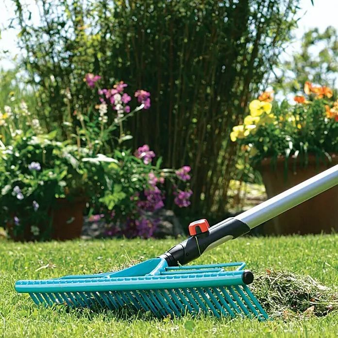 Gardena Combisystem Rasenrechen - Arbeitsbreite: 60 cm, Stahl - Nahaufnahme eines blauen Gartenrechens auf Rasen mit Pflanzen im Hintergrund.