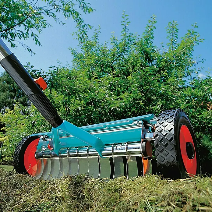 Gardena Combisystem VertikutierboyArbeitsbreite: 32 cm, Geeignet für: Moos- und Rasenfilzentfernung - Eine Nahaufnahme eines Rasenlüfters mit Rädern und Metallklingen vor einem grünen Garten.