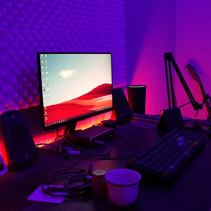 Briloner LED-Band Flexband - Länge: 5 m, Lichtfarbe: RGBW, 22 W - Lebendiger Computer-Schreibtisch mit Monitor, Lautsprechern, Tastatur und Mikrofonständer, beleuchtet von lila-rotem Licht vor Akustikschaumwand.