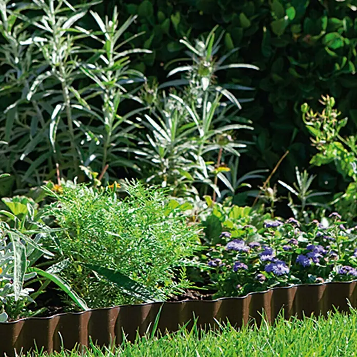 Gardena Beeteinfassung - 9 m x 20 cm, Schwarz - Nahaufnahme einer flexiblen braunen Rasenkante, die einen Garten mit verschiedenen Pflanzen und grünem Gras abgrenzt.