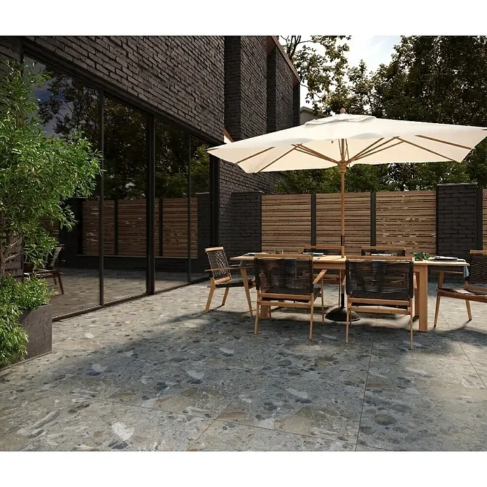 Feinsteinzeugfliese Vogue - 60 x 60 cm, Grey, Matt - Graue und mehrfarbige Terrassenfliesen in Steinoptik bilden einen einladenden Essbereich im Freien mit Tisch, Stühlen und Sonnenschirm.