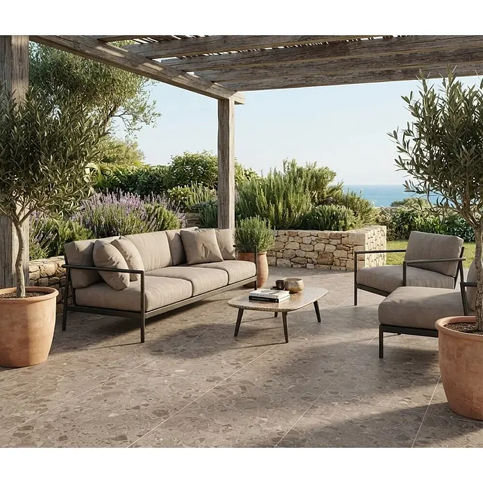 Feinsteinzeugfliese Vogue - 60 x 60 cm, Brown, Matt - Moderne Outdoor-Sofa und Sessel mit dunklem Rahmen und hellen Kissen auf einer gefliesten Terrasse unter einer Pergola, umgeben von Pflanzen und Meerblick.