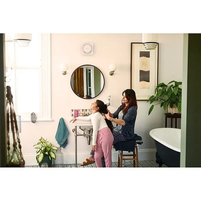 Bosch Wandventilator Fan 1900 DH W 125 - Weiß, Durchmesser Anschluss: 12,5 cm, Mit Lichtschalter + Feuchtigkeitssensor + Nachlauf - Weißes quadratisches Badlüftergerät mit konzentrischen Kreisen, an der Wand über dem Spiegel montiert.
